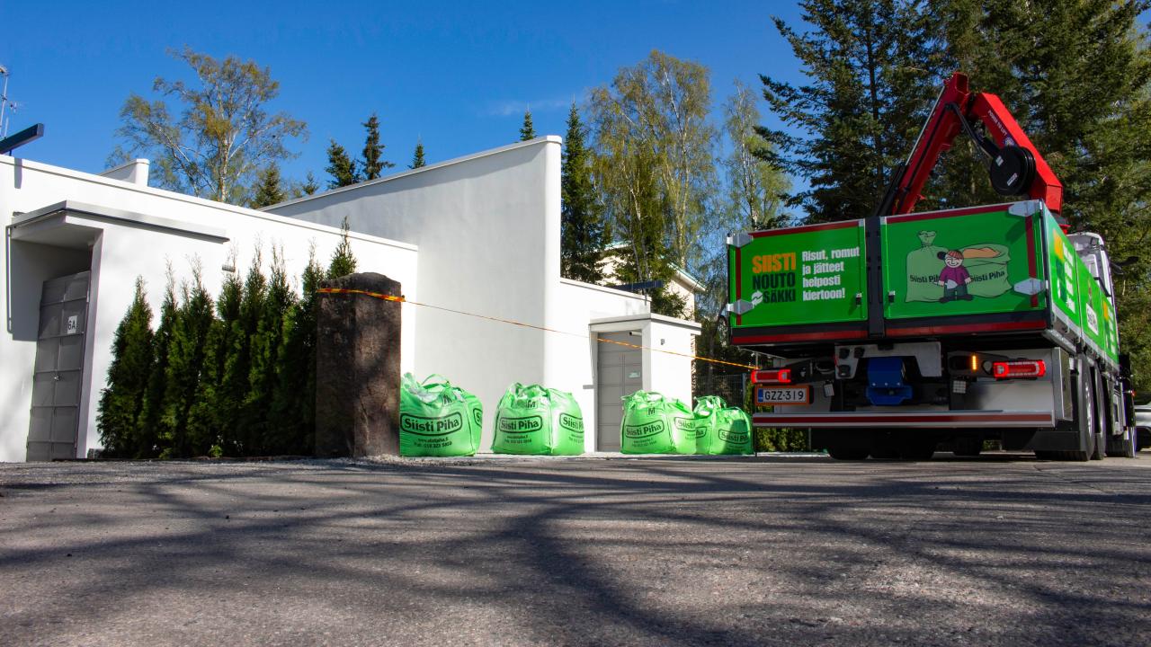 Suomen Siisti Piha Oy vihreä suursäkki kuorma-auto noutamassa suursäkkejä valkoisen talon edestä