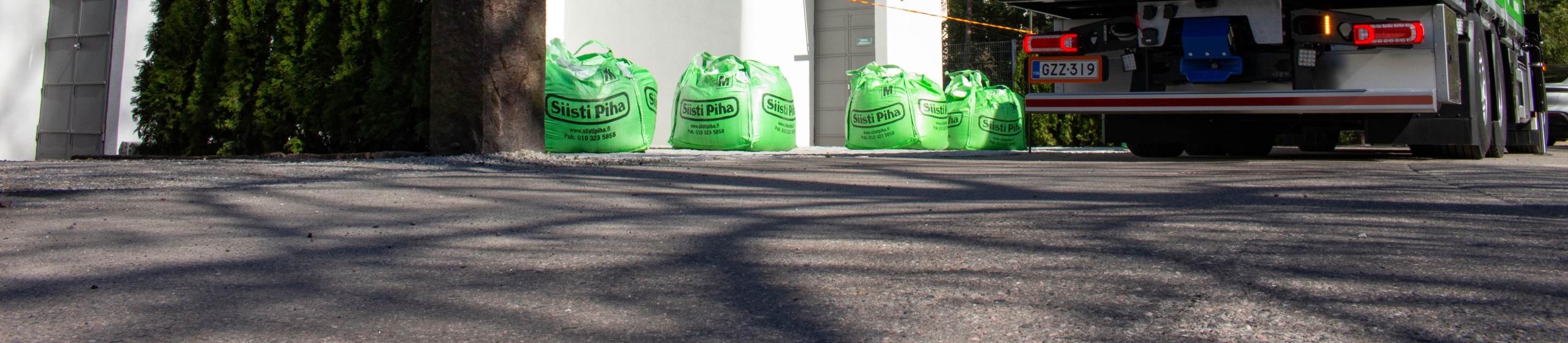 Suomen Siisti Piha Oy vihreä suursäkki kuorma-auto noutamassa suursäkkejä valkoisen talon edestä